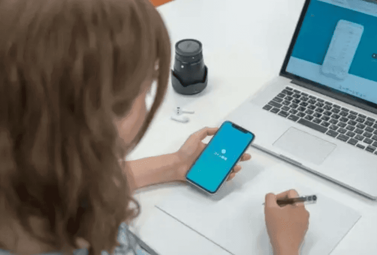A woman holding a phone with a wallet app beside a laptop