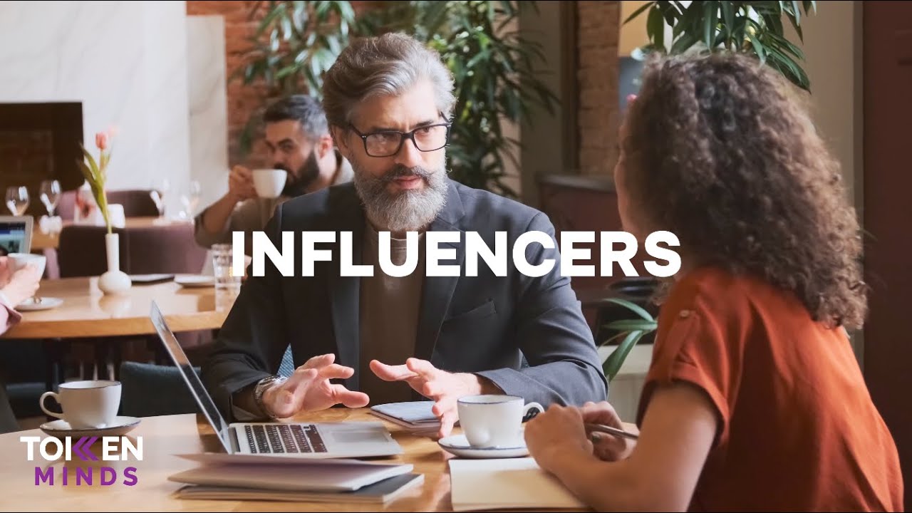 Influencers: a bearded man in glasses talks with a woman over coffee and a laptop in a cafe