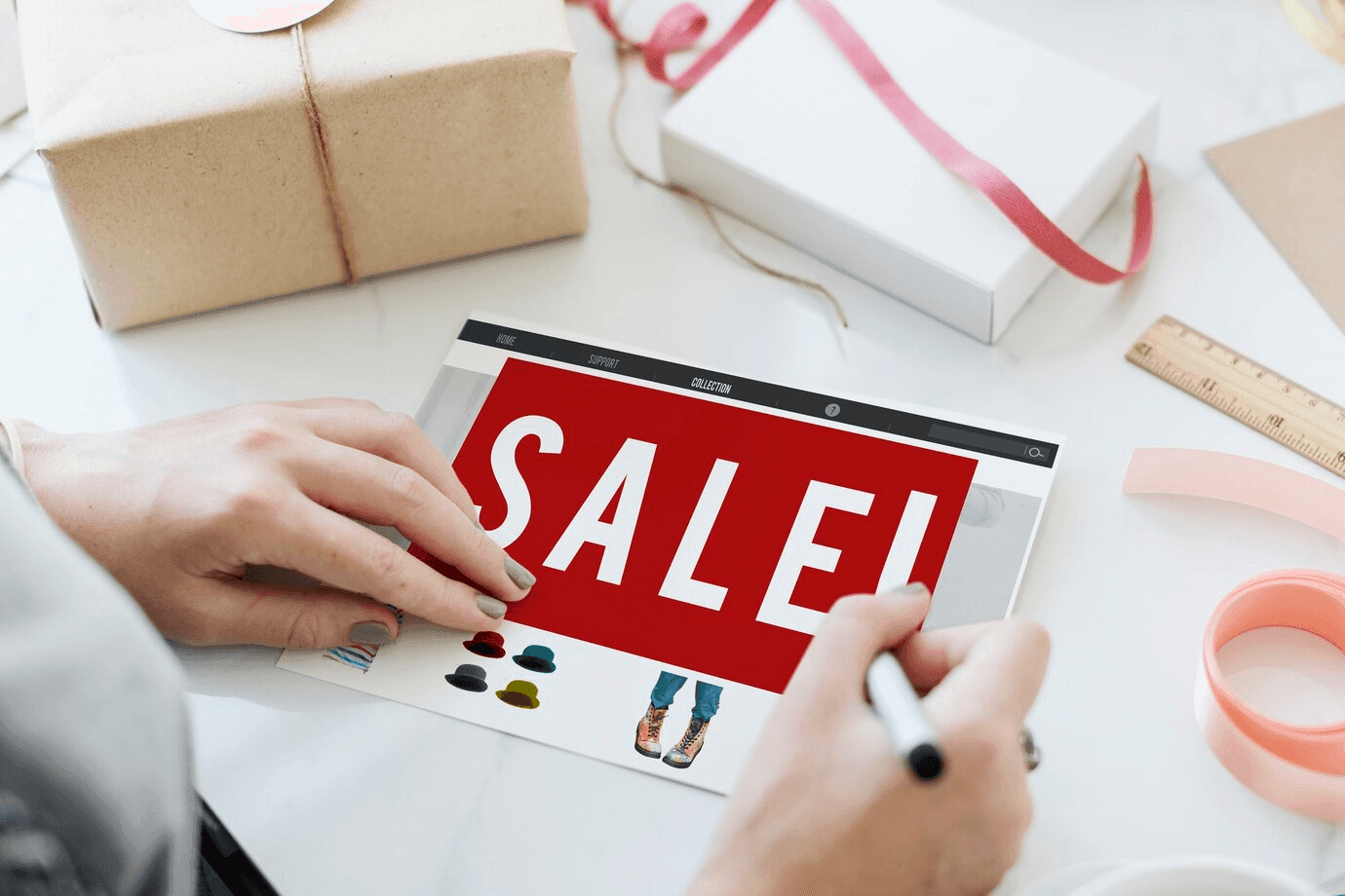 Hands marking a SALE! catalogue page beside wrapped gift boxes
